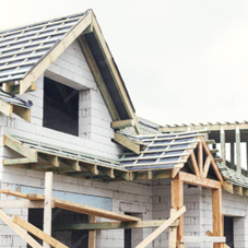 Kostka brukowa i kamień ozdobny - Domek jednorodzinny w trakcie budowy. Budynek murowany z białych bloczków, z widoczną drewnianą konstrukcją dachu.